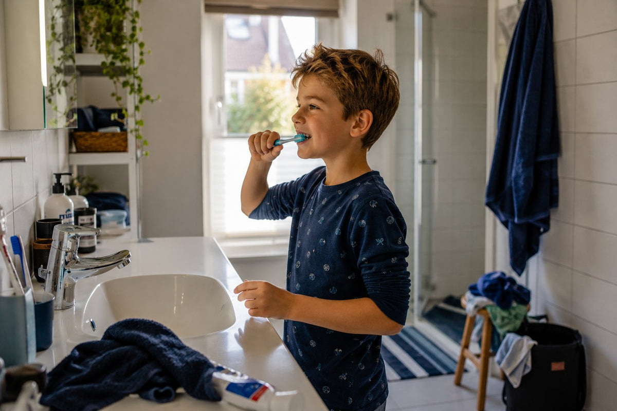 Jongen in pyjama poetst zelf zijn tanden bij de wastafel